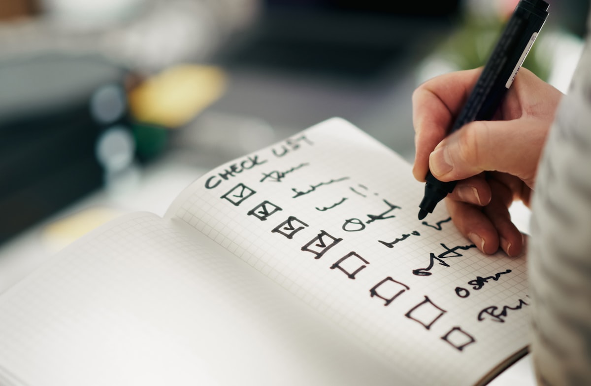 Close-up of a hand writing and checking off items on a handwritten checklist in a notebook